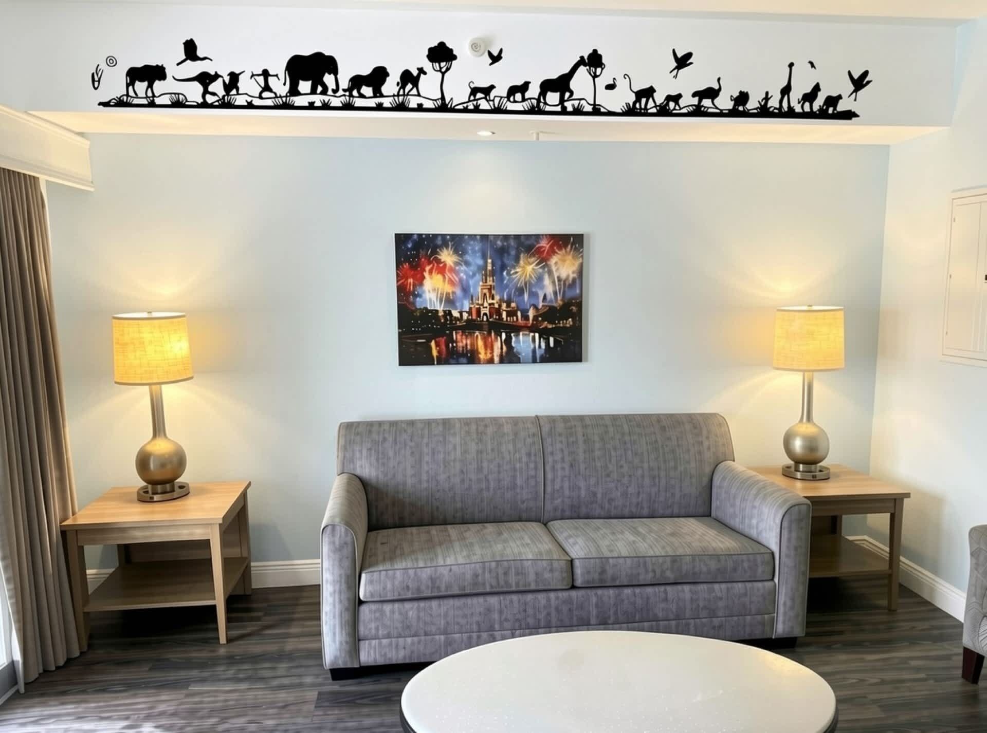 Uma sala de estar com um sofá cinza, duas mesas laterais com luminárias, uma pintura na parede de fogos de artifício e um mural no teto retratando a evolução da vida selvagem.