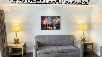 Uma sala de estar com um sofá cinza, duas mesas laterais com luminárias, uma pintura na parede de fogos de artifício e um mural no teto retratando a evolução da vida selvagem.