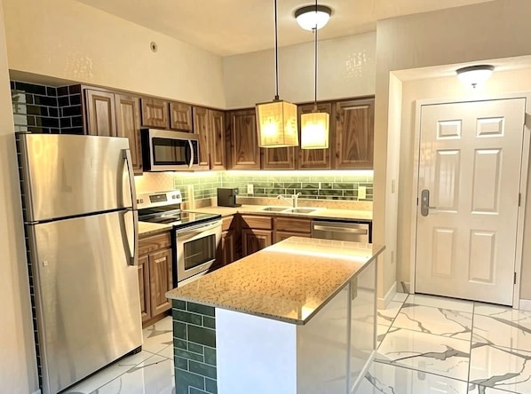 Una cocina moderna con electrodomésticos de acero inoxidable, armarios de madera, una isla de encimera de granito e iluminación colgante.