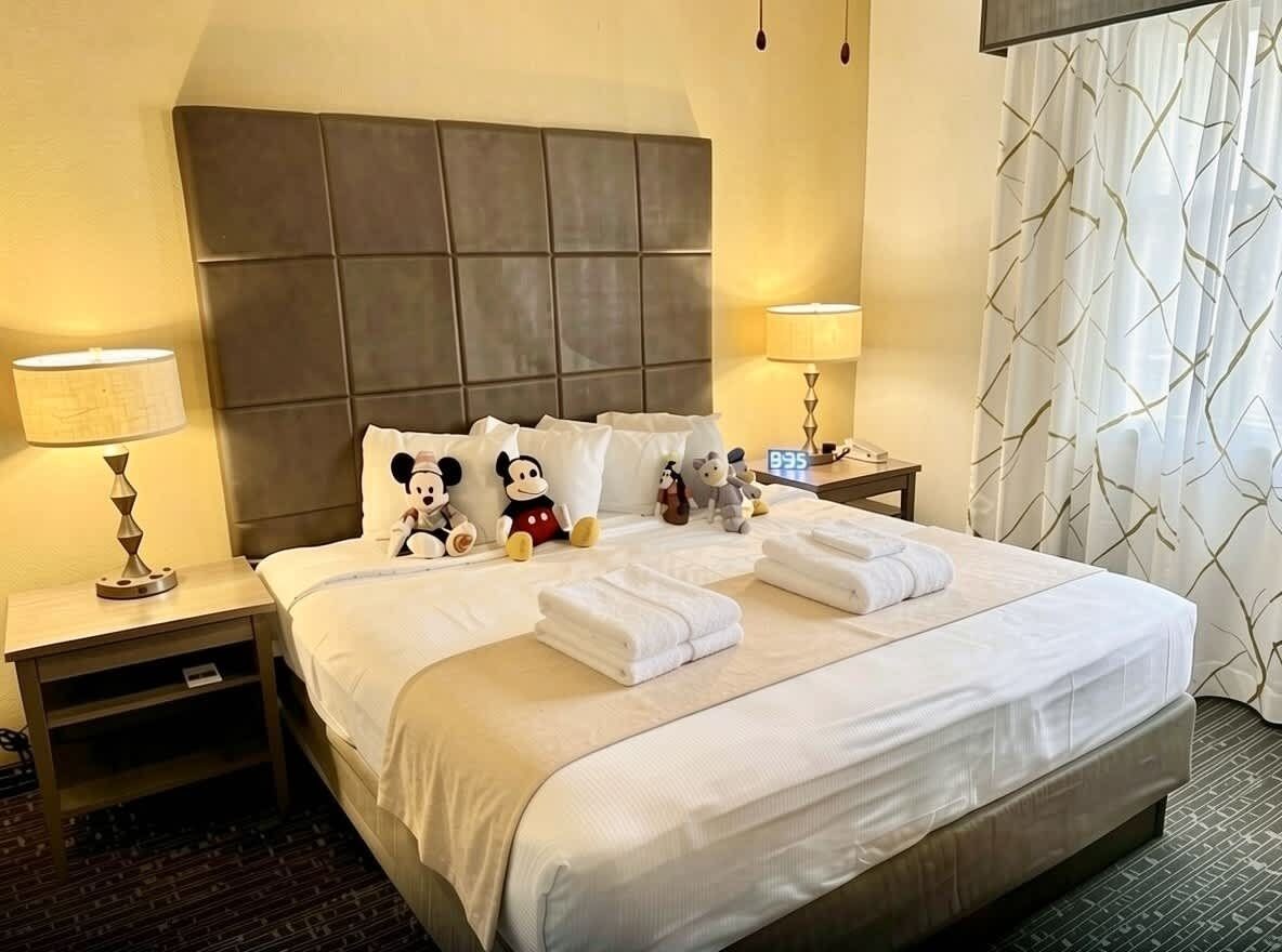 A hotel room with a large bed, two bedside tables, a headboard, and a window with curtains.