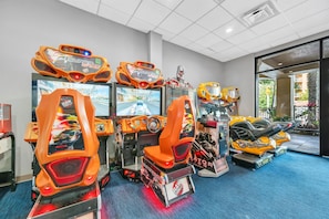 Una hilera de juegos de carreras de arcade con la marca 'Super Cars', un amplio ventanal con vista a la vegetación y un suelo cubierto de alfombra azul.
