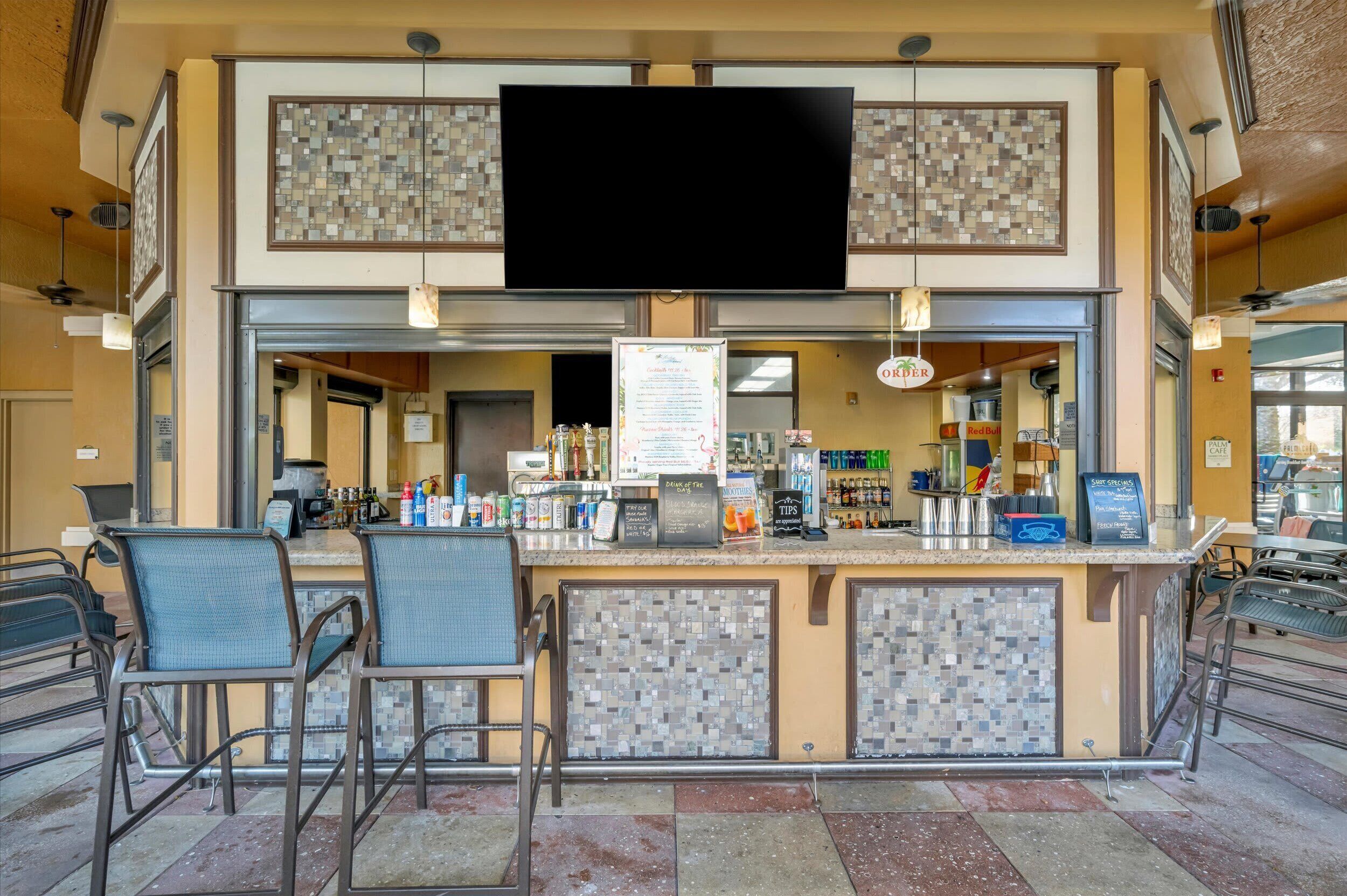 Uma área de bar com painel de azulejos, uma televisão de tela plana e um quadro de cardápio.