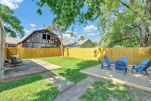 A backyard with a wooden fence, a concrete patio, and blue Adirondack chairs.