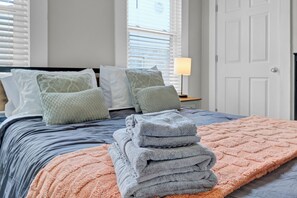 Un lit bien fait, avec des oreillers, une pile de serviettes pliées et une couverture sur un lit doté d’une tête de lit.