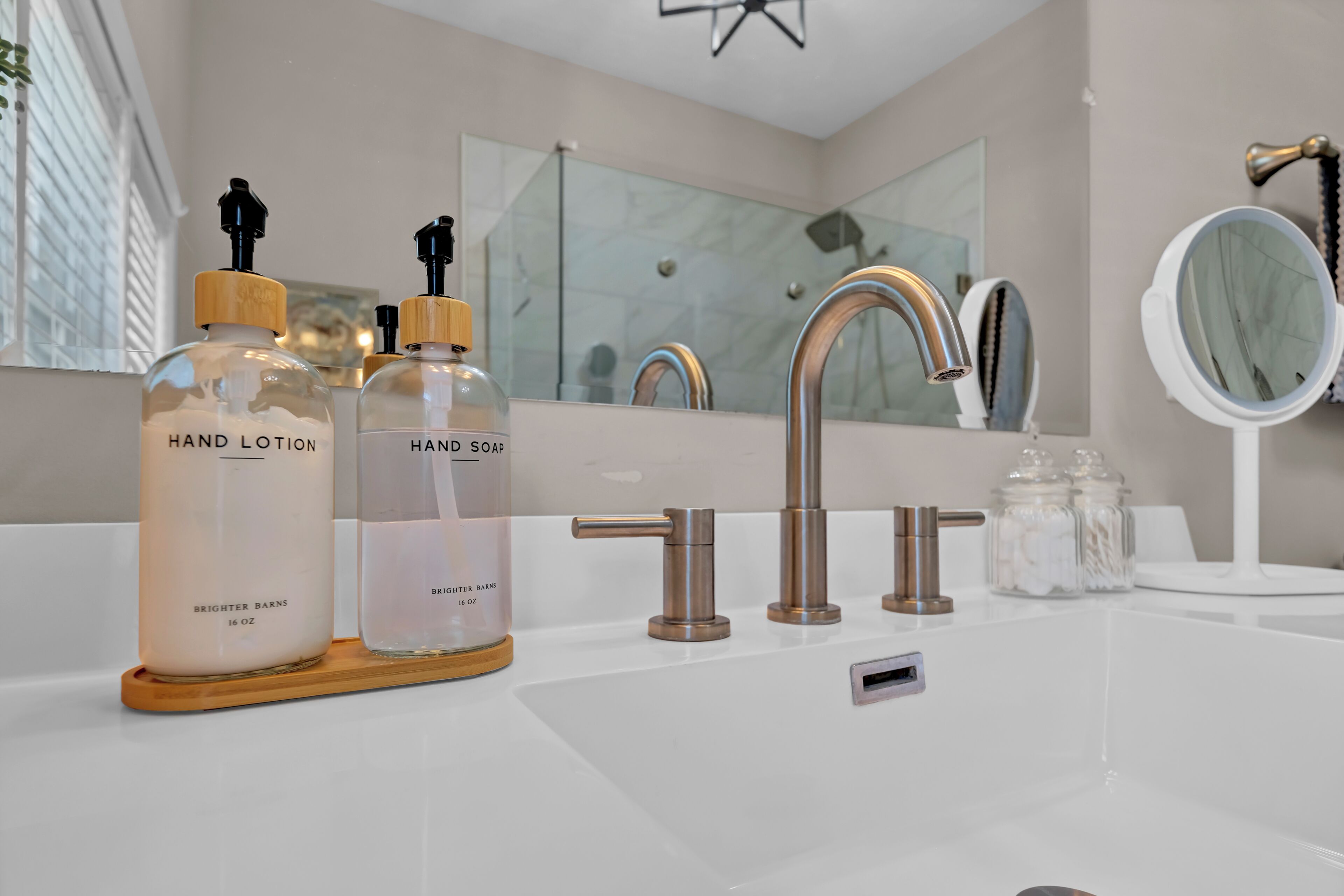 Ein Badezimmer mit einem weißen Waschbecken, zwei Flaschen Handlotion, einer Handseifenflasche, einem modernen Wasserhahn und einem Spiegel.