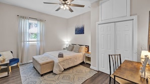 A bedroom with a bed, bedside tables, a desk, a chair, a ceiling fan, and a door. - Sleeps 8 • Fenced Yard and Firepit • 8 Minutes to Louisville (Jeffersonville)