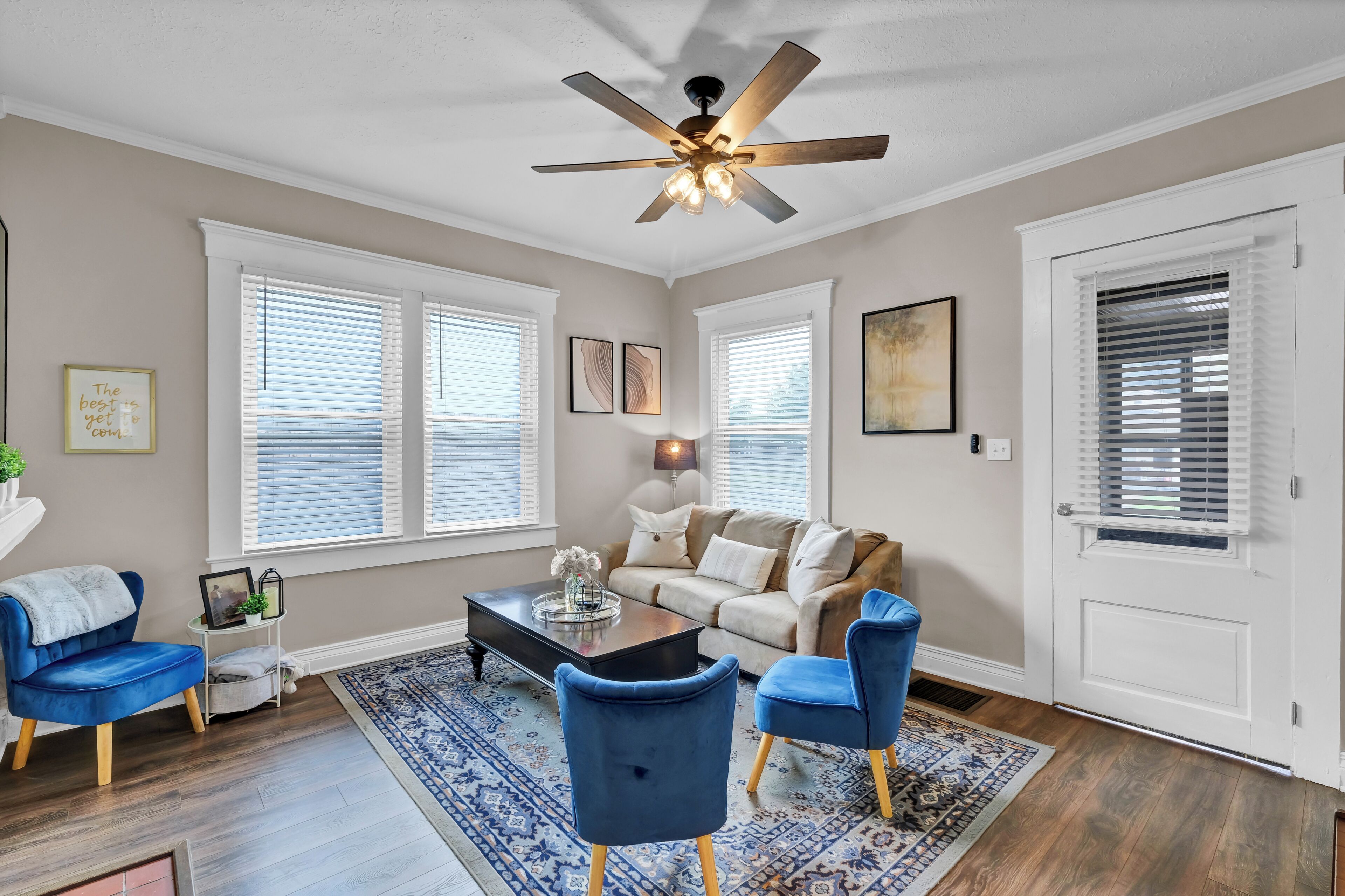 A living room with a ceiling fan, a sofa, two blue chairs, a coffee table, and a patterned rug.