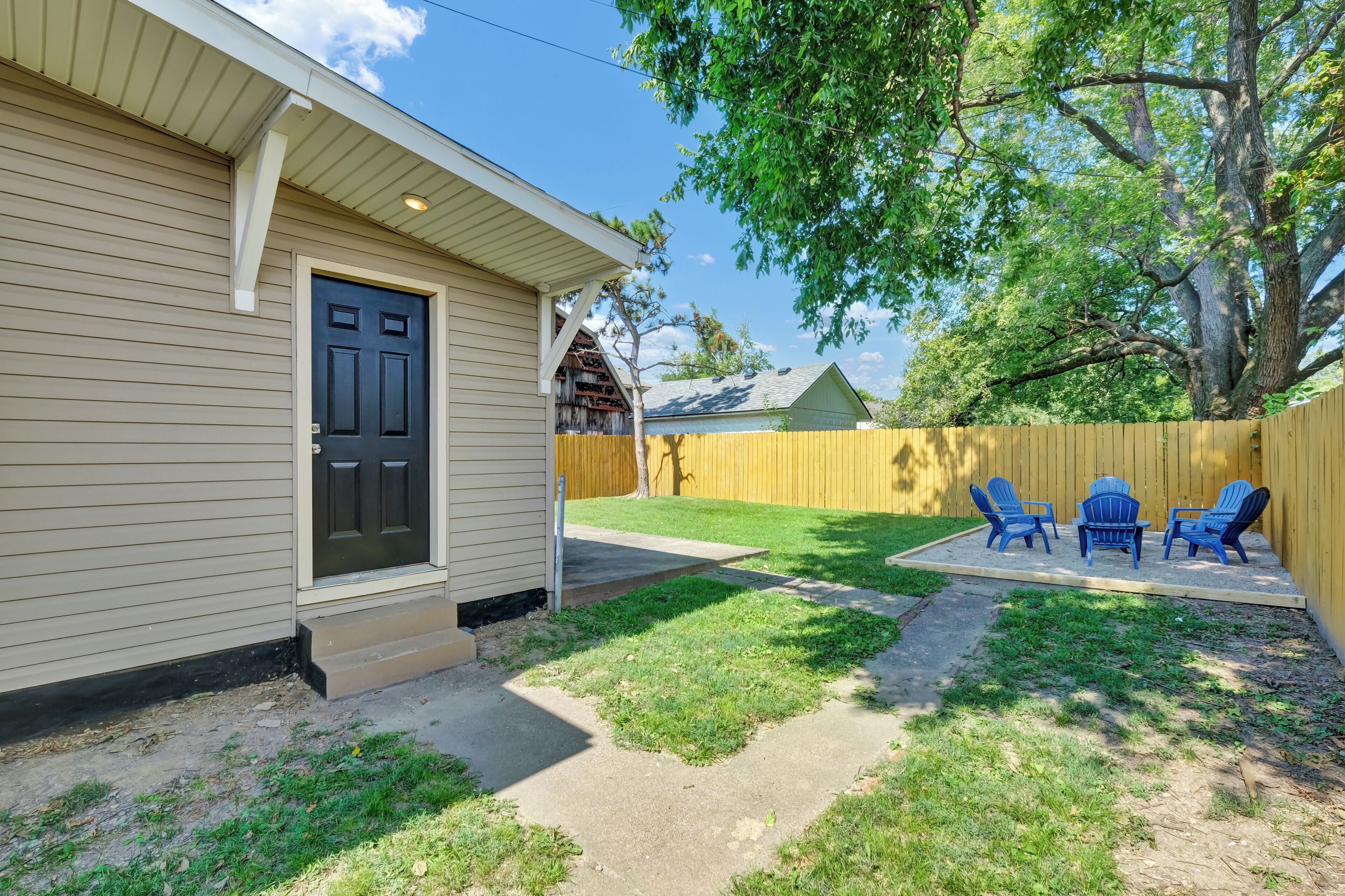 Una vivienda con puerta principal, un pequeño porche, patio trasero cercado y mobiliario exterior.