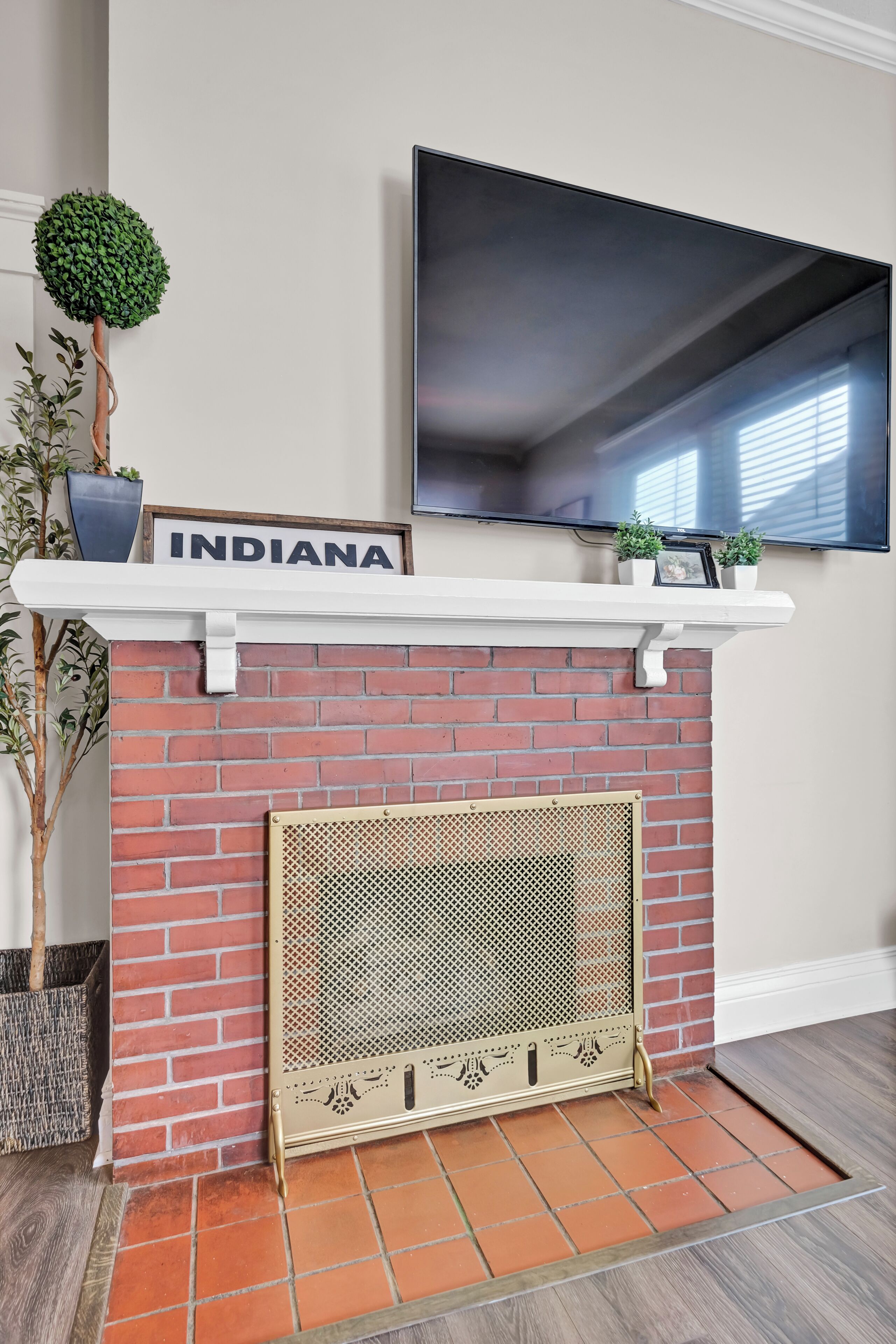 A fireplace with a brick wall, a mounted TV above it, and a sign that reads 'INDIANA' on the mantel.