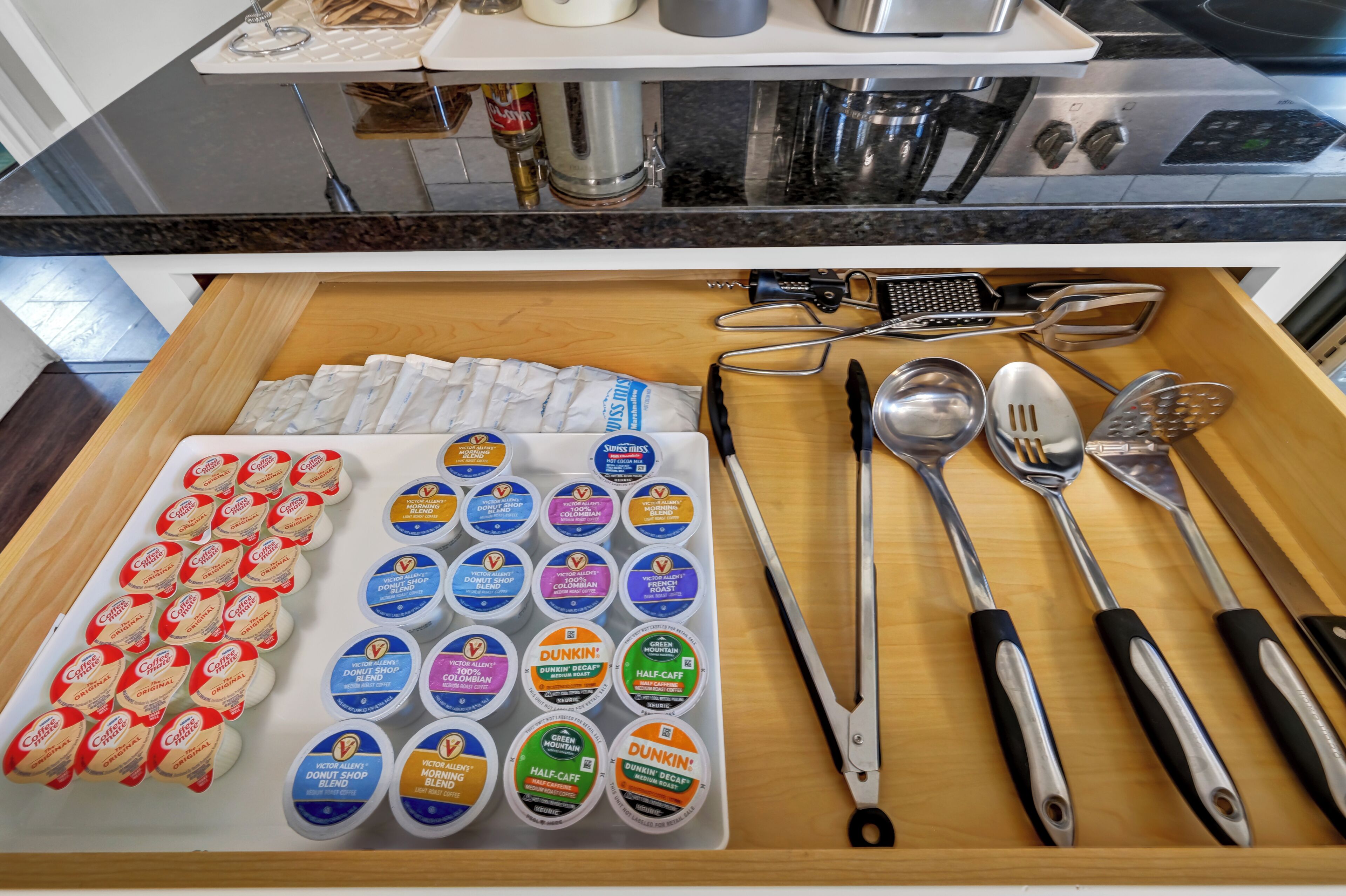 A kitchen counter with coffee pods, a grater, and various utensils.