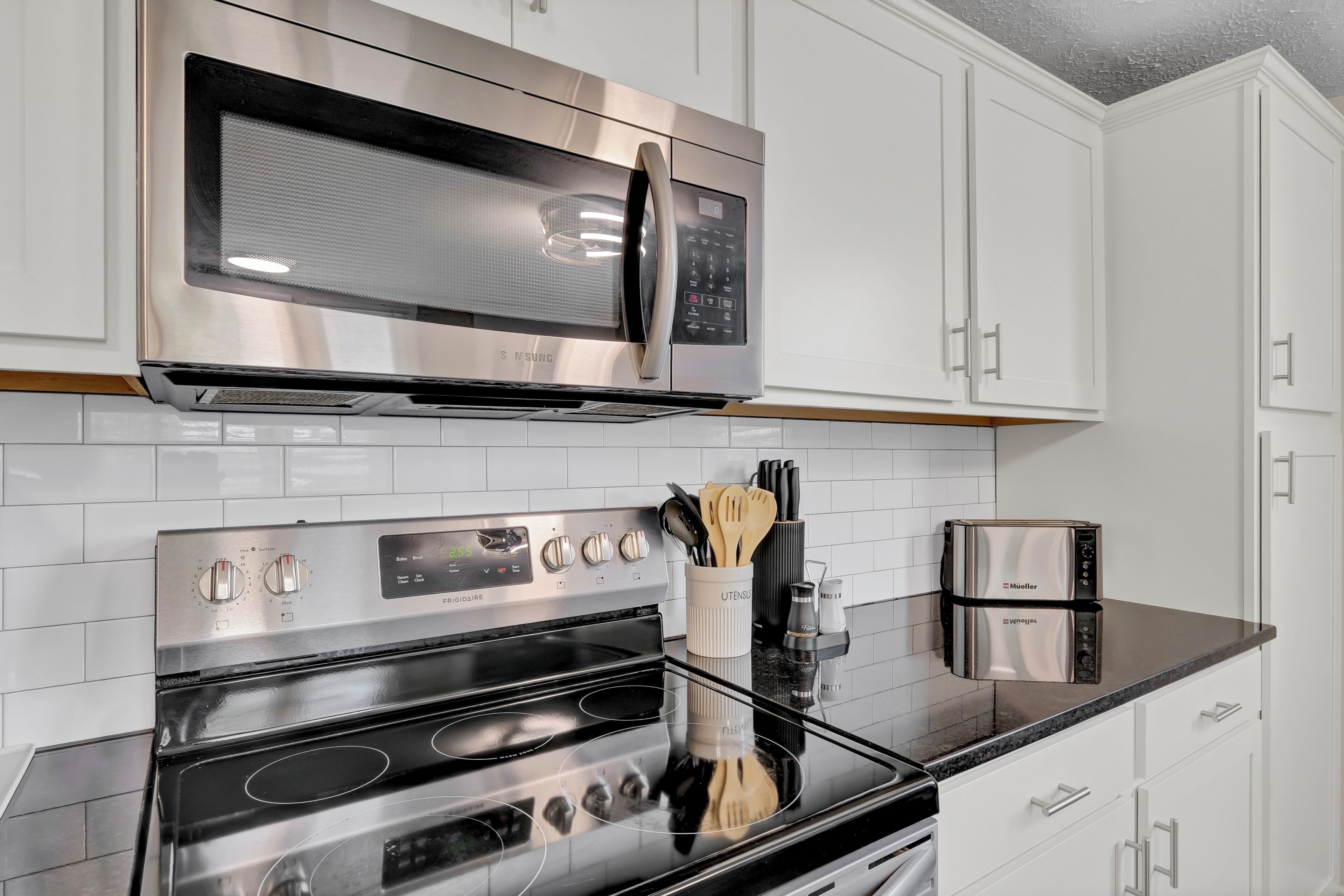 Una cucina con elettrodomestici in acciaio inossidabile, tra cui un forno a microonde e un forno, armadietti bianchi e un piano di lavoro nero.