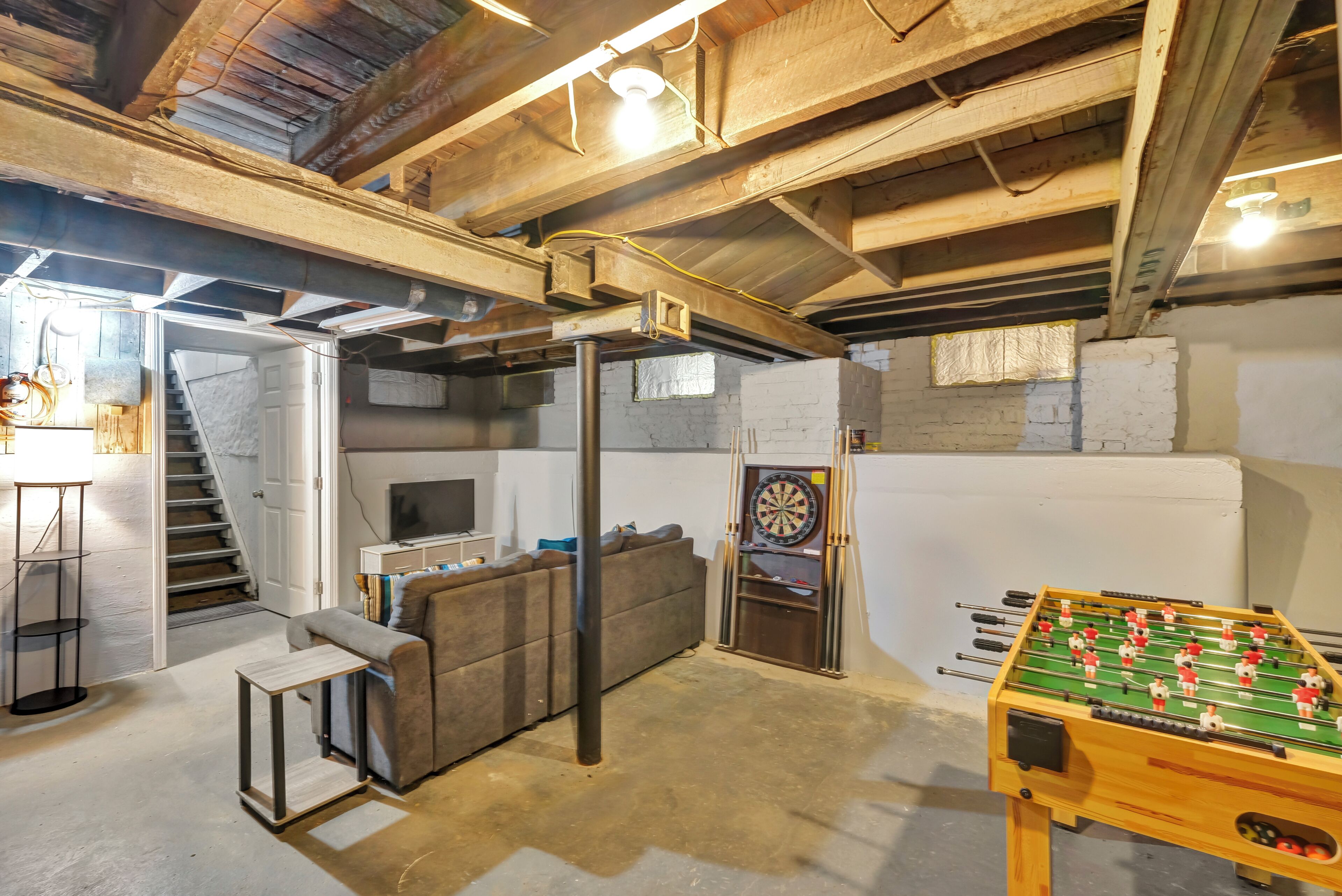 A room with a sofa, a dartboard, and a foosball table.