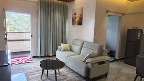 Sala de estar com sofá, mesa de centro, quadro e porta que dá para uma varanda.