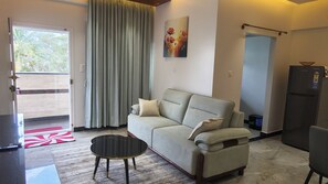 Un soggiorno con divano, tavolino, un quadro e una porta che dà su un balcone.
