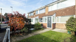 A two-story residential building with a brick facade, a front door, and a small front yard with grass and a tree with autumn leaves. - Peaceful hideaway with Homely Comforts (Greater Manchester)