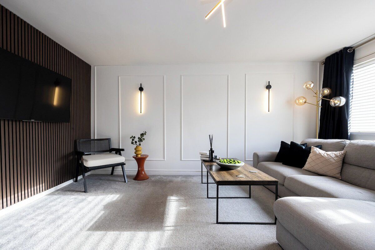 Uma sala de estar moderna com um sofá, uma mesa de centro, uma televisão e luminárias decorativas na parede.