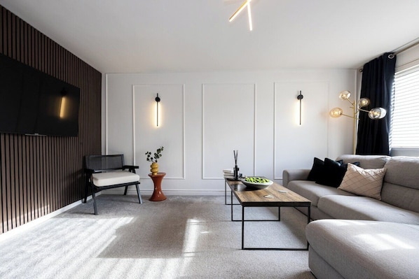 Una sala de estar moderna con un sofá, una mesa de centro, un televisor e iluminación decorativa en la pared.