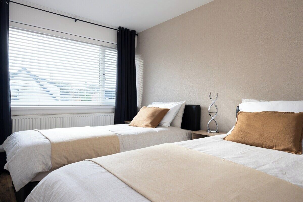 Quarto de hotel com duas camas, um radiador, uma janela com persianas e um alto-falante fixado na parede.