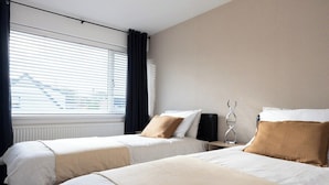 A hotel room with two beds, a radiator, a window with blinds, and a wall-mounted speaker. - Peaceful hideaway with Homely Comforts (Greater Manchester)