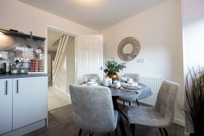 Una cocina moderna con estufa integrada, un área de comedor con mesa dispuesta para dos personas y una escalera que conduce a otro nivel.