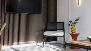 Un salon moderne avec un téléviseur à écran plat fixé au mur, un fauteuil noir avec un coussin blanc, un mur lambrissé en bois, une petite table orange et une plante en pot aux feuilles jaunes et vertes.