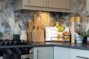 A kitchen with a marble backsplash, wooden cutting board, and a cookbook.