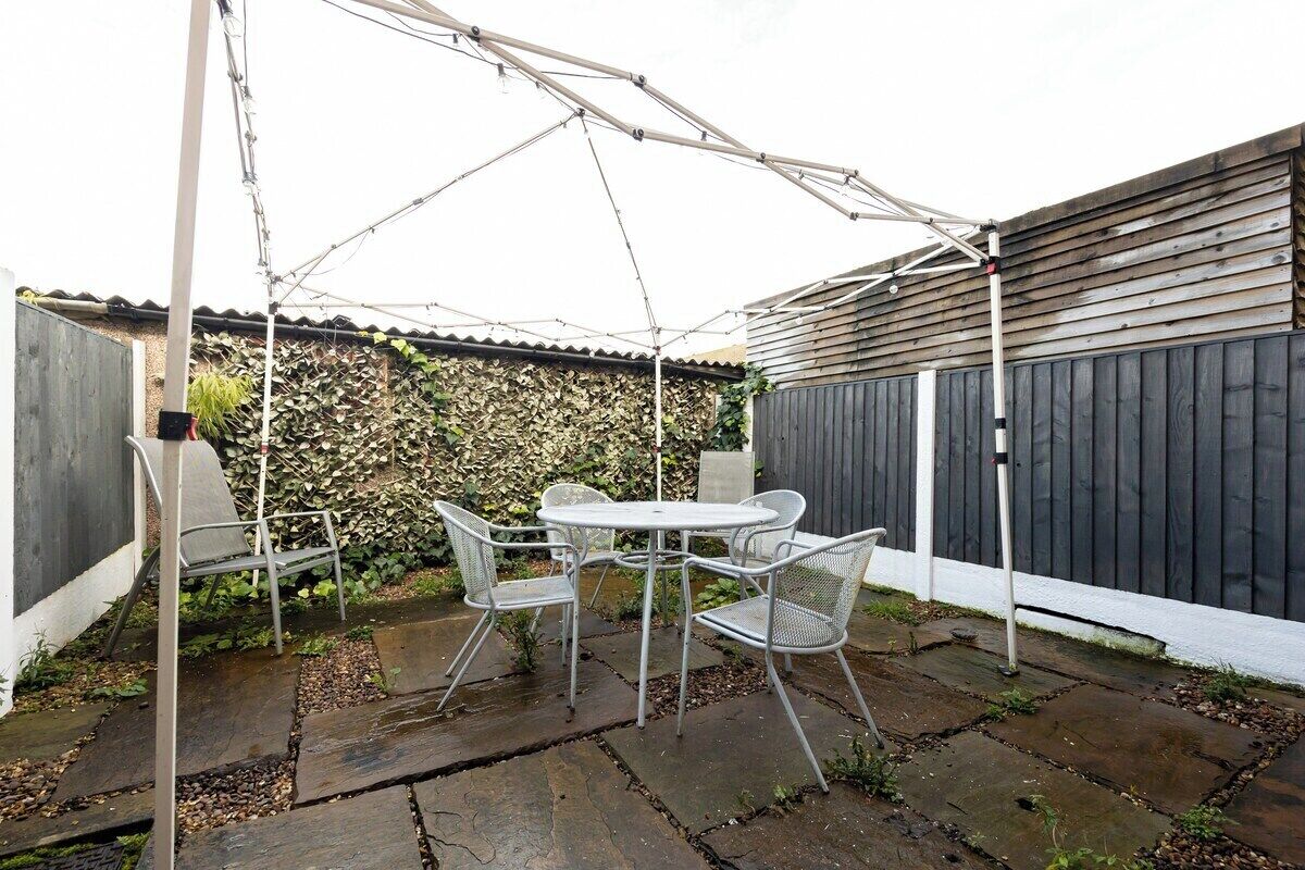 Um pátio externo com mesa, cadeiras, um guarda-sol branco e cerca de madeira.