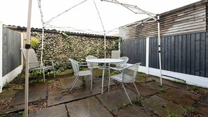 An outdoor patio with a table and chairs, a white umbrella, and a wooden fence. - Peaceful hideaway with Homely Comforts (Greater Manchester)
