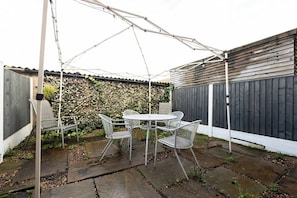 Un patio al aire libre con una mesa, sillas, un paraguas blanco y una valla de madera.