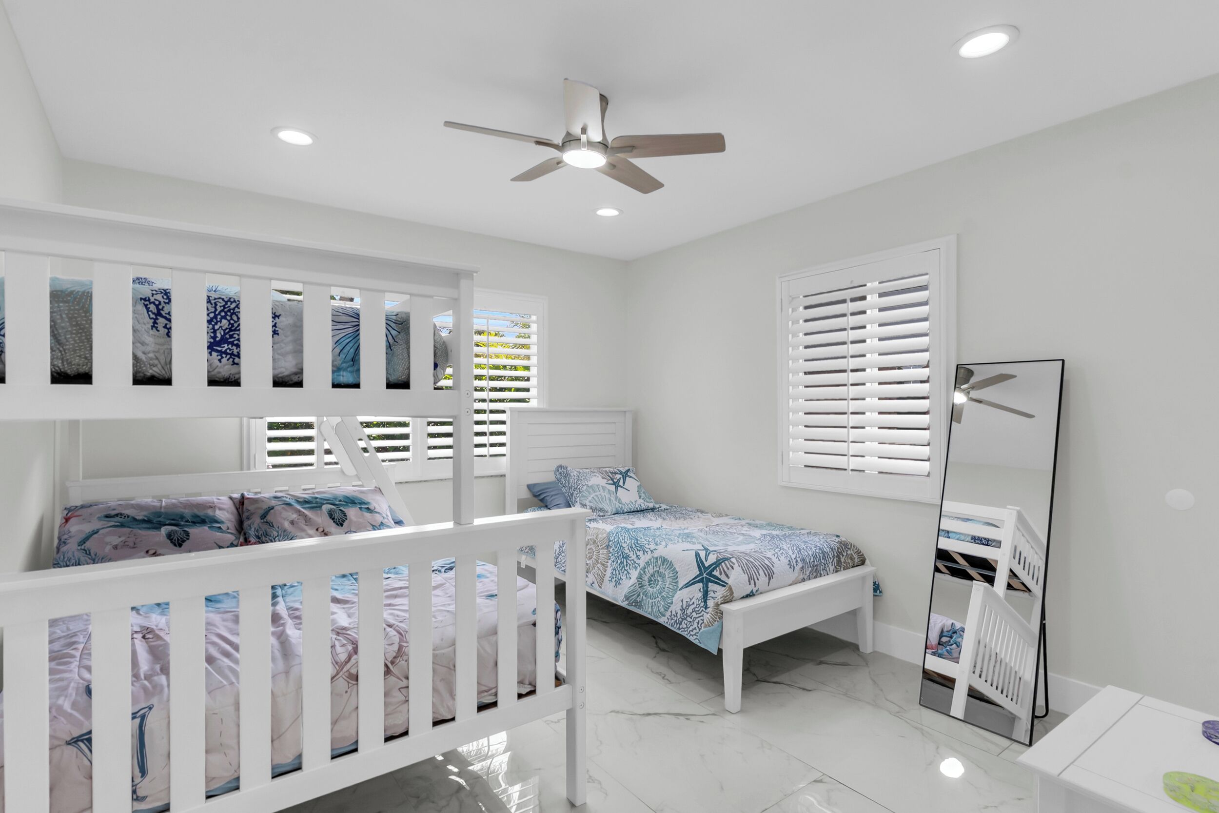 Une chambre d’enfant avec des lits superposés, un ventilateur de plafond et un grand miroir.