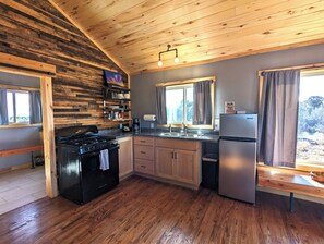 A kitchen with wooden walls, a stove, cabinets, a refrigerator, and a window with curtains.