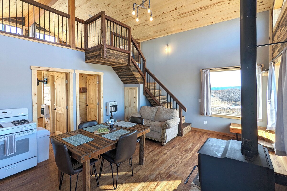 A spacious kitchen with a stove, dining table, and chairs. A staircase leads to an upper level with a balcony.