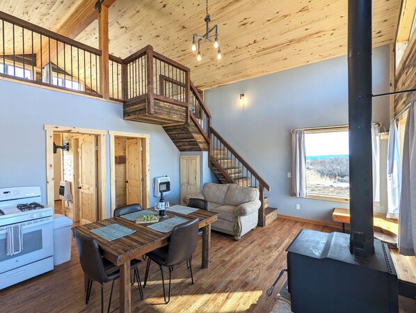 A spacious kitchen with a stove, dining table, and chairs. A staircase leads to an upper level with a balcony. - Wolf Springs Ranch (La Sal)