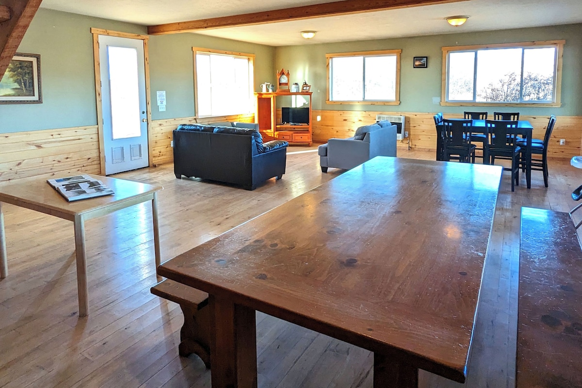 A spacious living area with a wooden dining table, sofas, and a staircase.