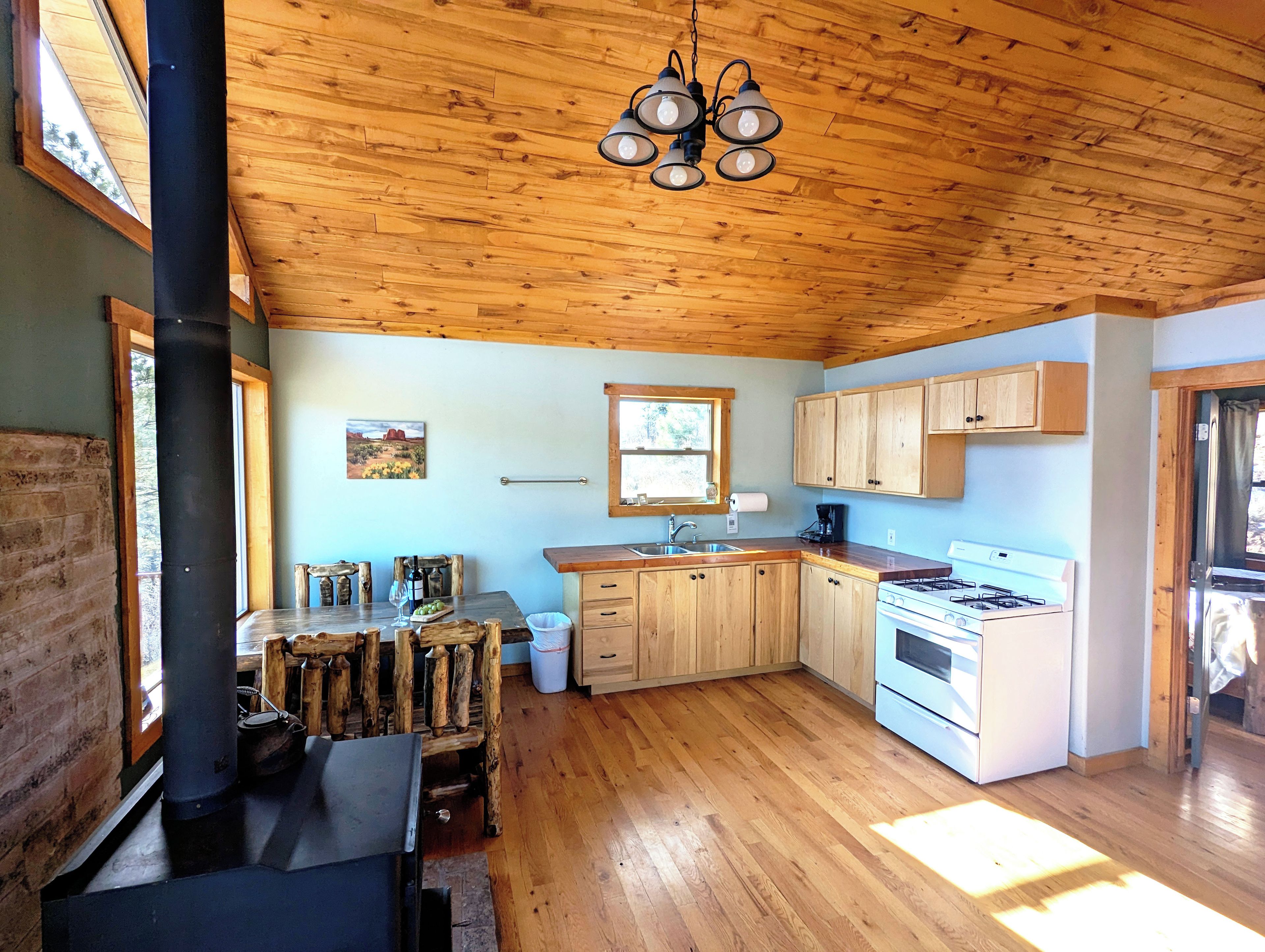 Une cuisine rustique avec des meubles de rangement en bois, un poêle et un coin repas comprenant une table et des chaises en bois.