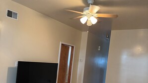 A room with a ceiling fan, a flat-screen TV on a stand, wooden flooring, and a door leading to another room. - Welcoming 2-bedroom building with AC in vibrant Chicago (Chicago)