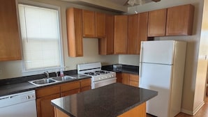 A kitchen with wooden cabinets, a granite countertop, a stove, a sink, and a refrigerator. - Welcoming 2-bedroom building with AC in vibrant Chicago (Chicago)
