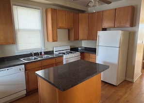 A kitchen with wooden cabinets, a granite countertop, a stove, a sink, and a refrigerator. - Welcoming 2-bedroom building with AC in vibrant Chicago (Chicago)