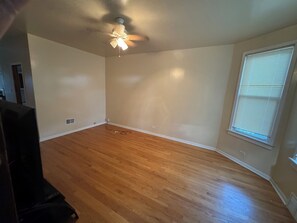 A room with hardwood flooring, a ceiling fan, a window with blinds, and a visible electrical outlet. - Welcoming 2-bedroom building with AC in vibrant Chicago (Chicago)