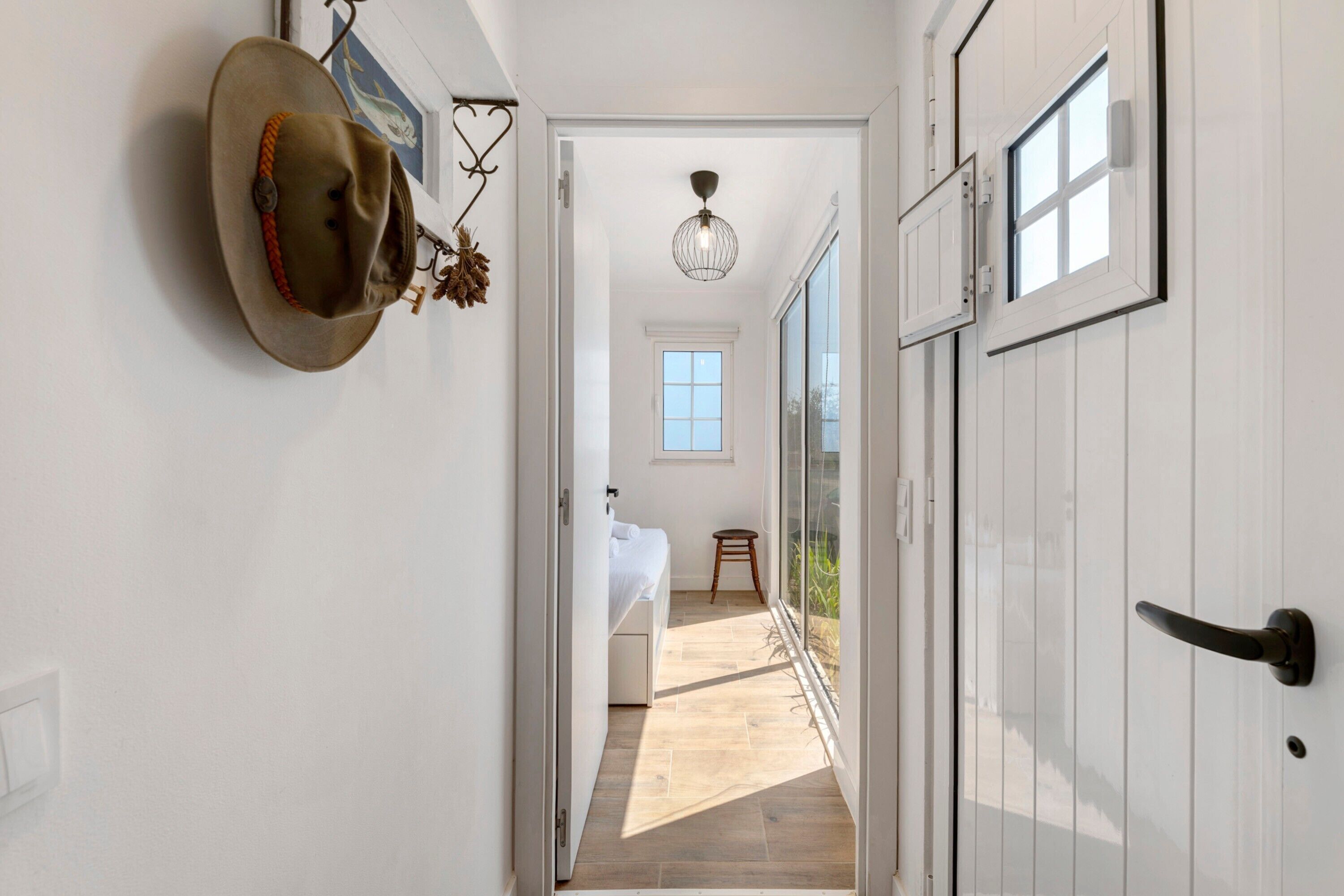 A hallway leading to a bedroom with a large window, a hanging hat, and a chandelier.
