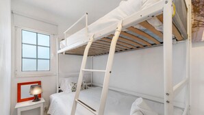 Une chambre avec un lit superposé, une fenêtre, une table de chevet avec une lampe et une serviette sur le lit.
