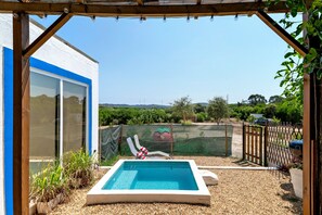 A swimming pool with a view of the countryside, a fenced area with chairs, and a building with large windows. - Holiday Home 'Oliveira Brava T2' with Mountain View, Private Pool and Wi-Fi (Porto Covo)