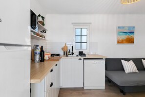 A compact kitchen with a dishwasher, a microwave, and a window above the sink. - Holiday Home 'Oliveira Brava T2' with Mountain View, Private Pool and Wi-Fi (Porto Covo)