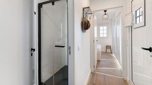 Un couloir avec une porte en verre, un porte-manteau avec des chapeaux, un luminaire suspendu et un plancher en bois.
