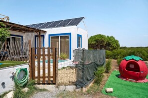 A house with a solar panel roof, a fenced yard, and a red playhouse. - Holiday Home 'Oliveira Brava T2' with Mountain View, Private Pool and Wi-Fi (Porto Covo)