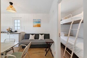 A compact room with a kitchenette, a sofa with pillows, a dining table with chairs, and a bunk bed. - Holiday Home 'Oliveira Brava T2' with Mountain View, Private Pool and Wi-Fi (Porto Covo)