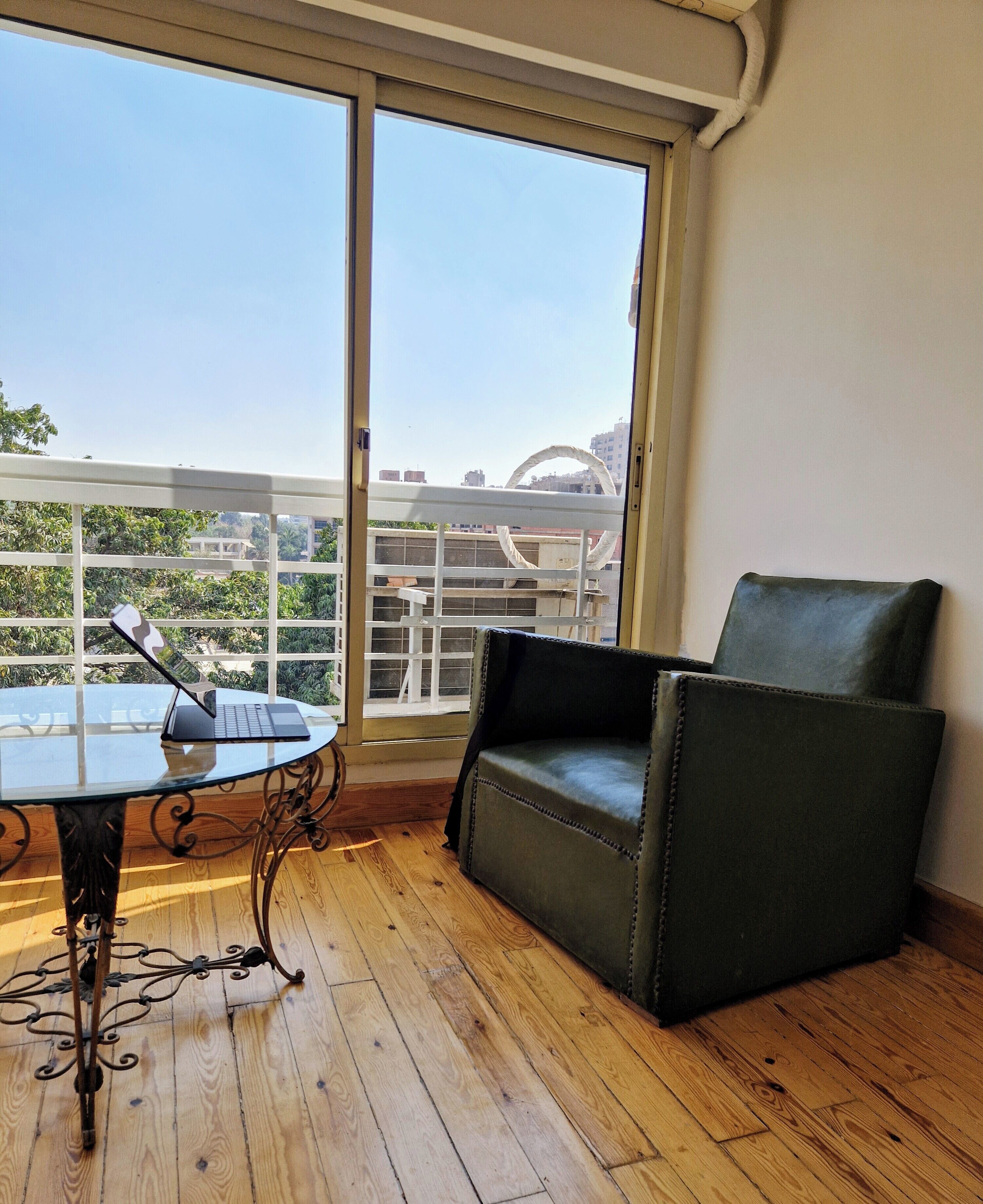 Ein Balkon mit Tisch und Stuhl, Holzboden und Blick auf Gebäude durch ein großes Fenster.