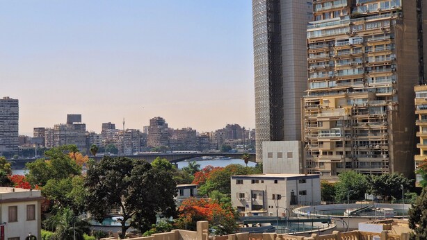 A high-rise building with multiple balconies and a river in the background. - Royal Retreat in Dokki • Spacious with Nile View (Giza Governorate)