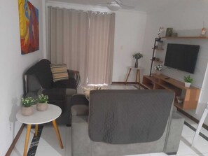A living room with a sofa, armchair, TV, and a painting on the wall.