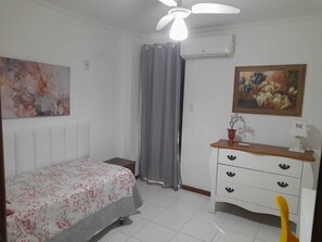 A bedroom with a bed, a dresser, a ceiling fan, an air conditioner, and a painting.